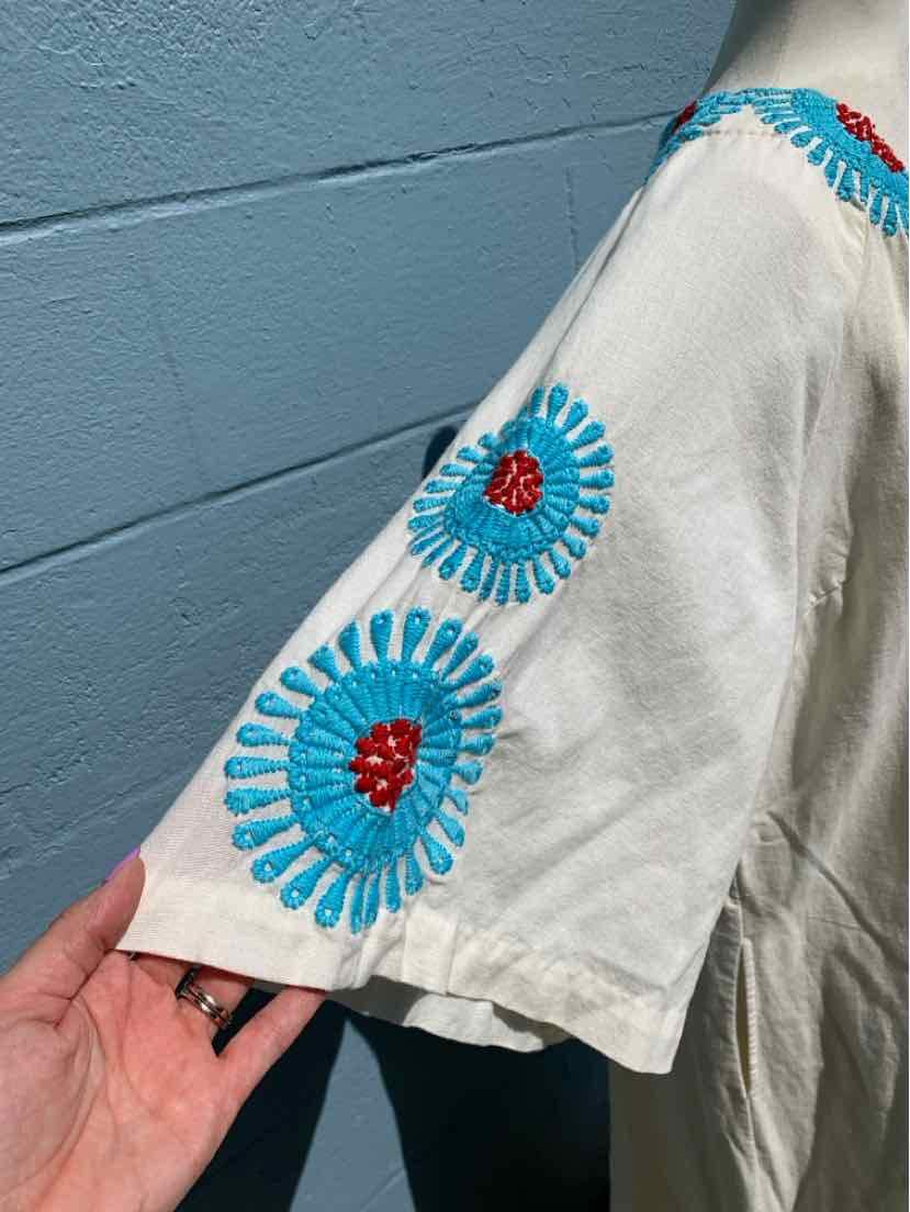 Cream short-sleeve top with blue and red circular embroidered patterns on the sleeve.