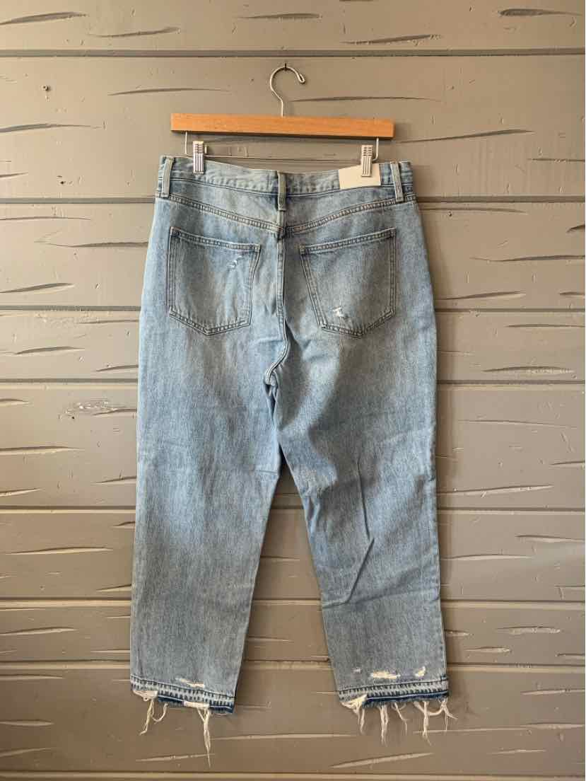 Light blue denim jeans with high waist and frayed hems hanging on wooden hanger against wooden wall.