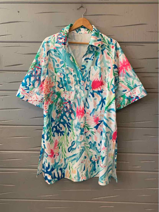 Short-sleeve collared shirt with abstract watercolor print in teal, pink, and coral on white background.