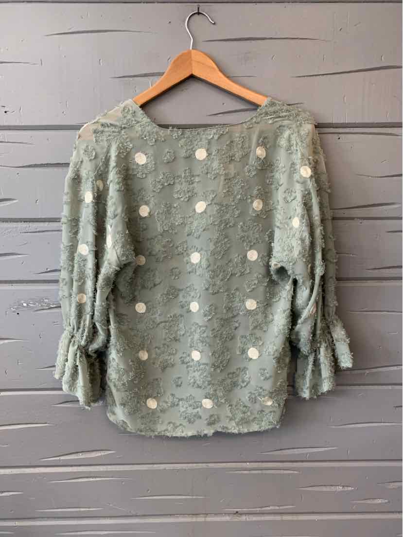 Light green textured blouse with white floral embroidery and gathered 3/4 sleeves on wooden hanger.