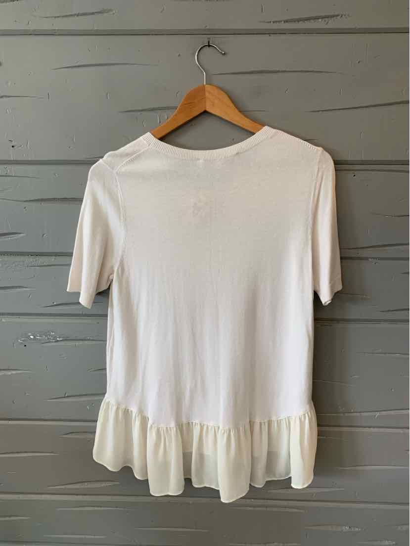 White short-sleeve top with round neckline and ruffled hem, hanging on wooden hanger.