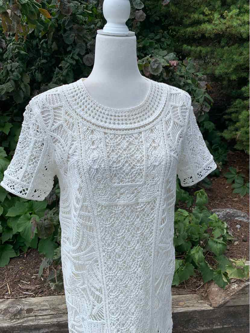 White short-sleeve knit dress with intricate lace-like patterns and round neckline on mannequin outdoors.