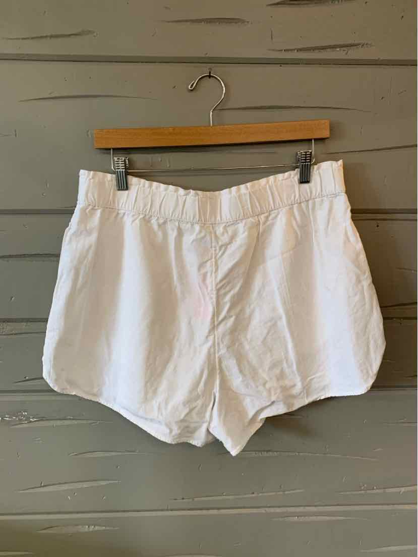 White high-waist shorts with elastic waistband and side pockets hanging on wooden hanger.