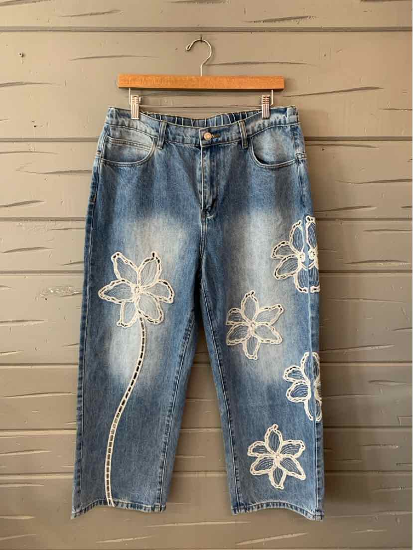 Light blue denim jeans with large white embroidered flower patches on front and relaxed fit.