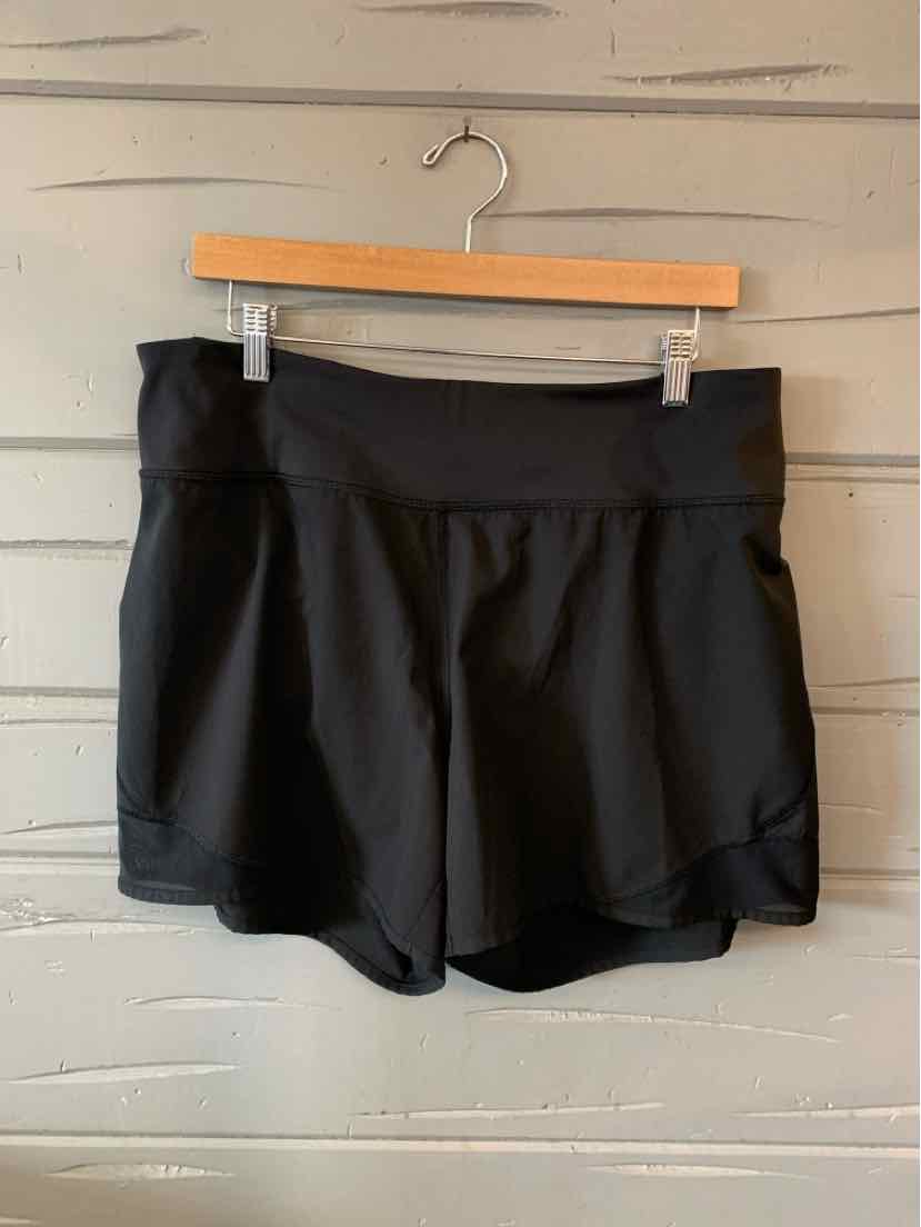 Black athletic shorts with wide waistband and loose fit, hanging on wooden hanger against gray wall.