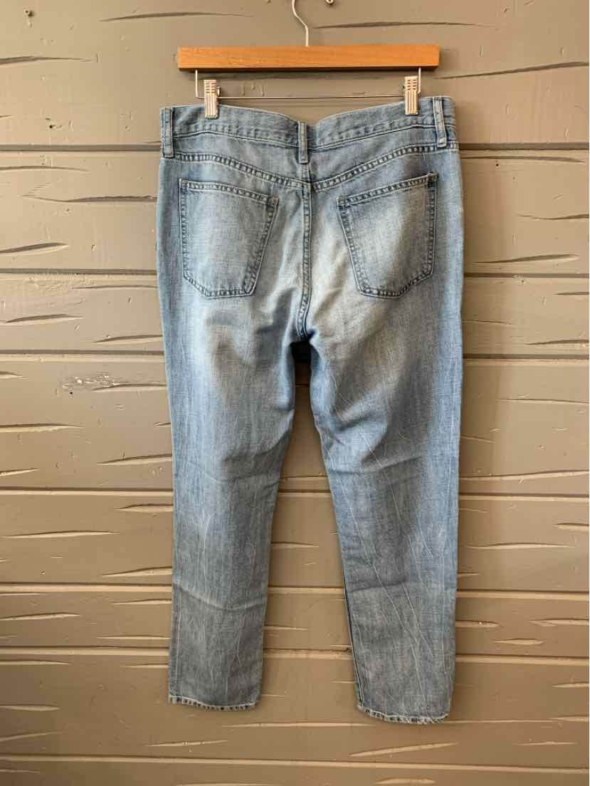 Light wash denim jeans with back pockets and slim straight legs hanging on wooden hanger against wooden panel wall.
