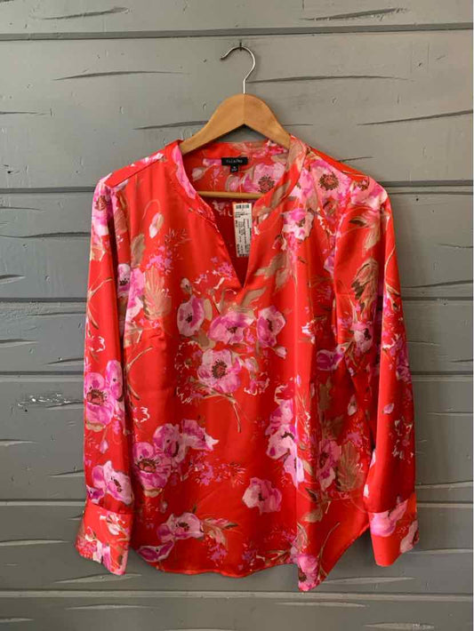 Pink long-sleeve blouse with bright floral print and V-neck on wooden hanger.