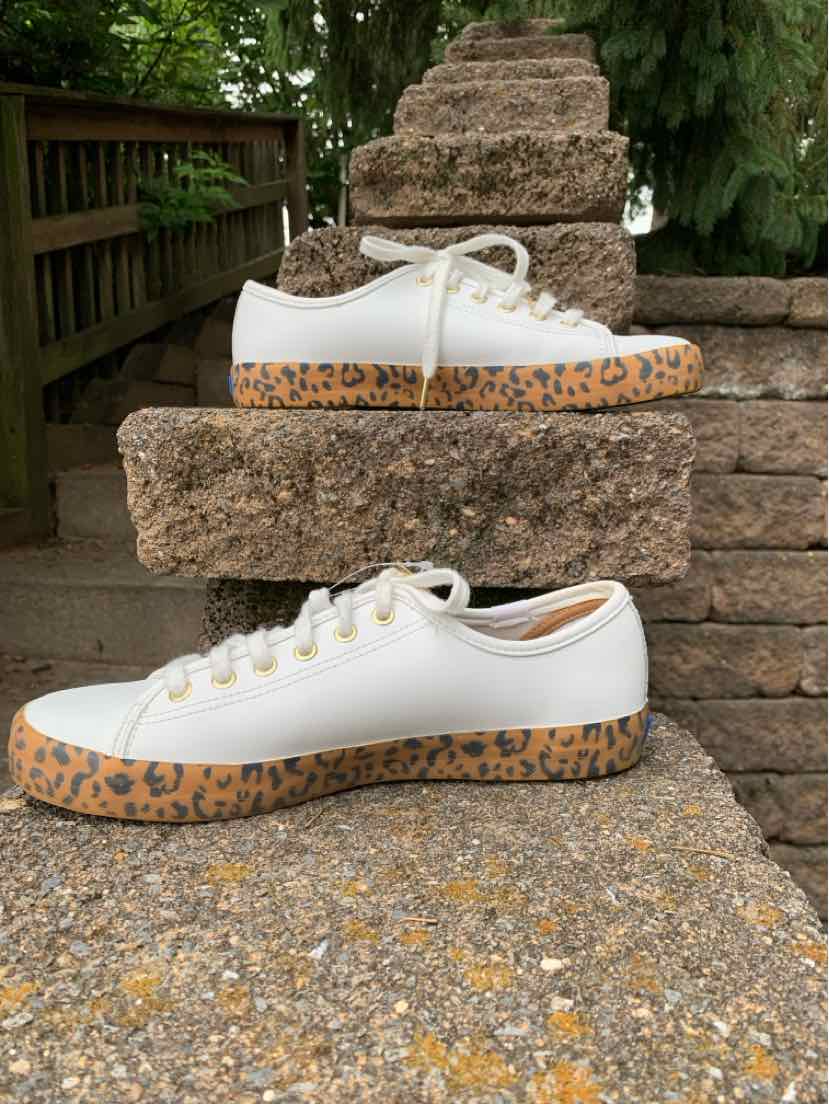 White low-top sneaker with white laces and a thick tan sole featuring black leopard spots.
