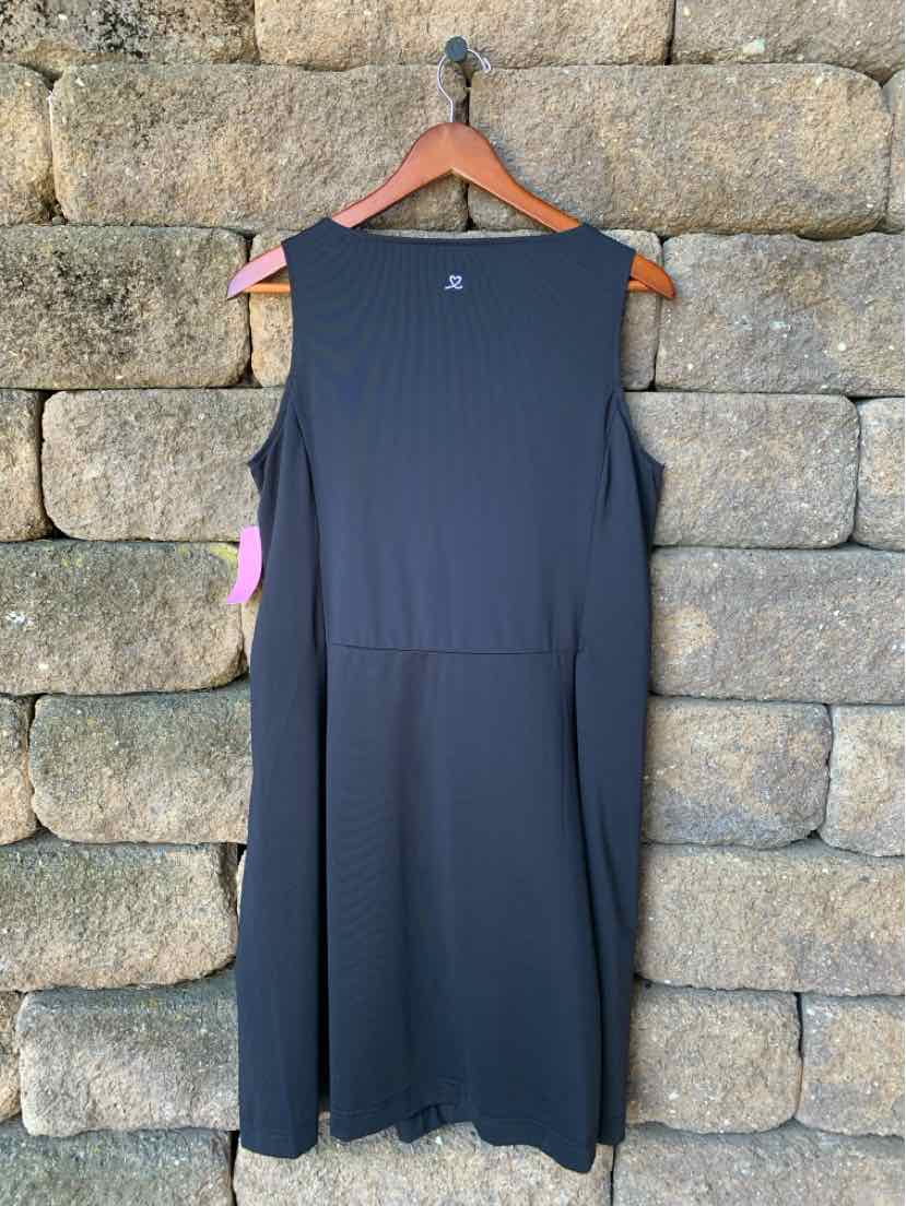 Black sleeveless sports dress with a straight cut and clean lines, medium size, hanging on wooden hanger against stone wall.