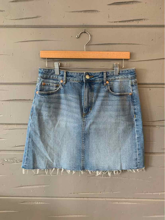 Light blue denim mini skirt with frayed hem and front pockets hanging on wooden hanger.