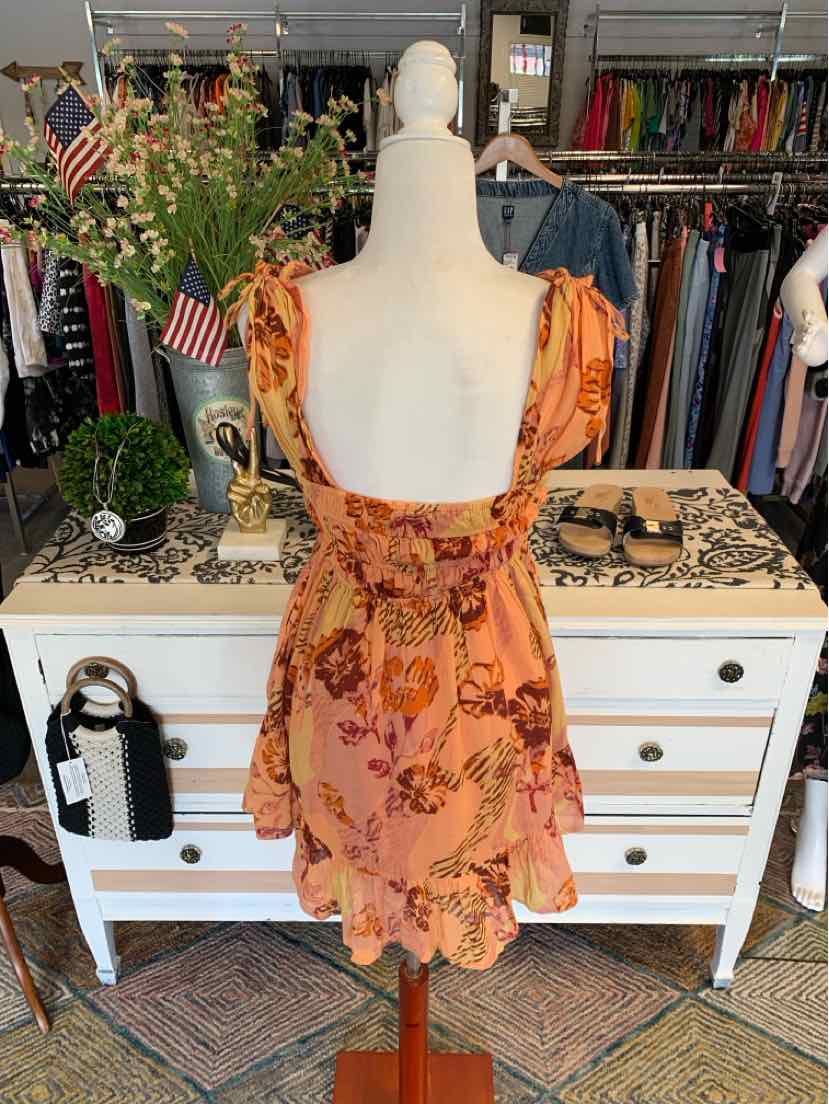 Peach-colored floral mini dress with ruffled straps and open back on mannequin.