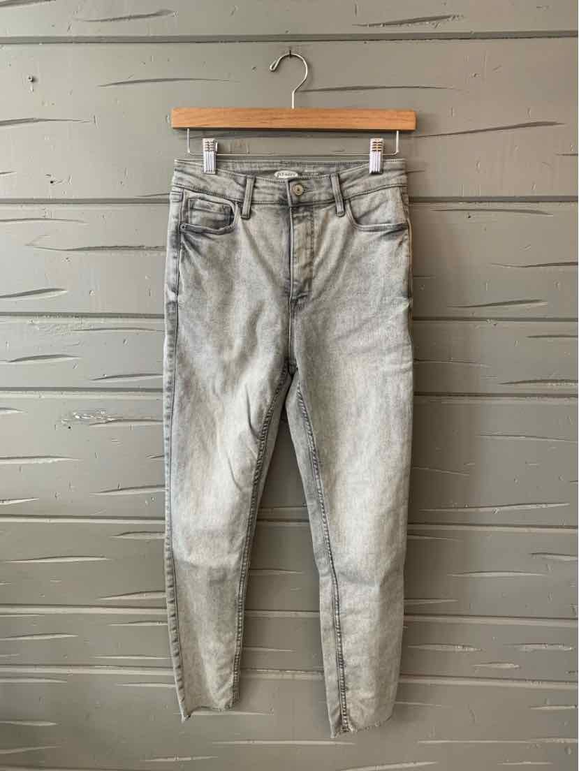Gray washed denim jeans with five pockets and skinny fit hanging on wooden hanger against textured gray wall.