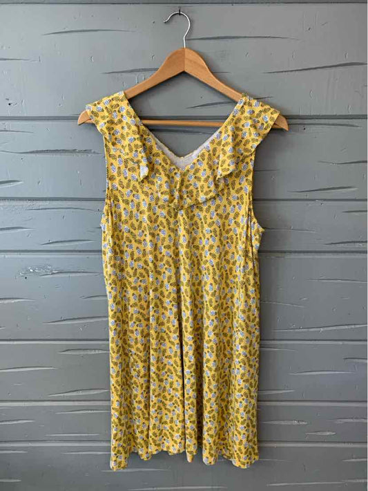 Yellow sleeveless dress with white floral pattern and a V-neck on wooden hanger against gray wall.