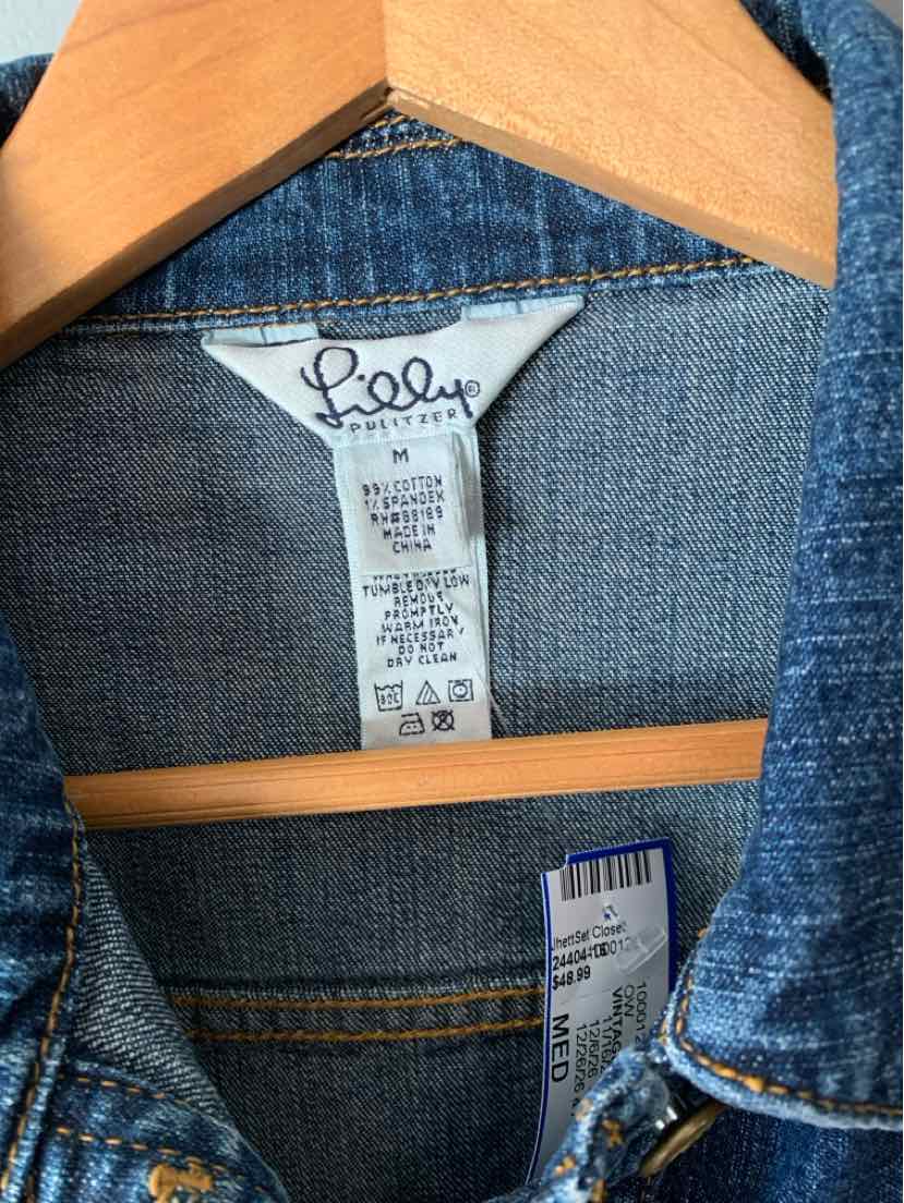 Blue denim Lilly Pulitzer garment with a white neck label and gold contrast stitching on a wooden hanger.
