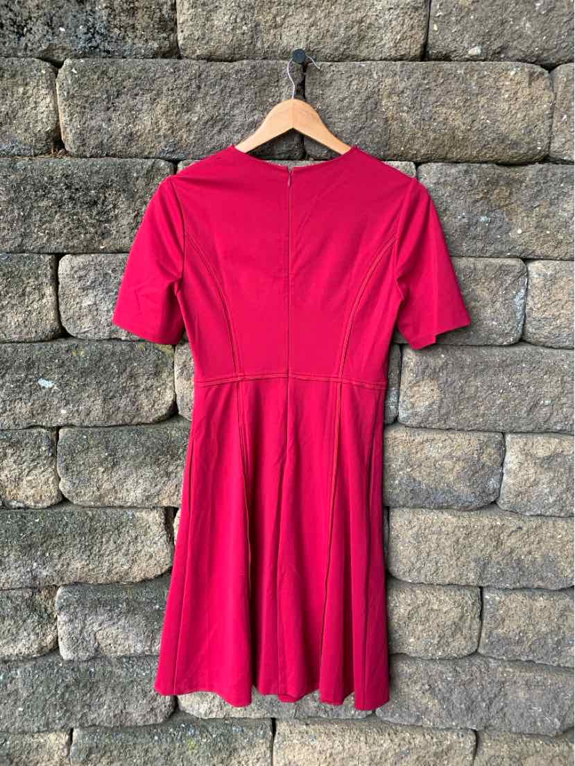 Pink short-sleeve dress with fitted bodice and flared skirt on wooden hanger against stone wall.