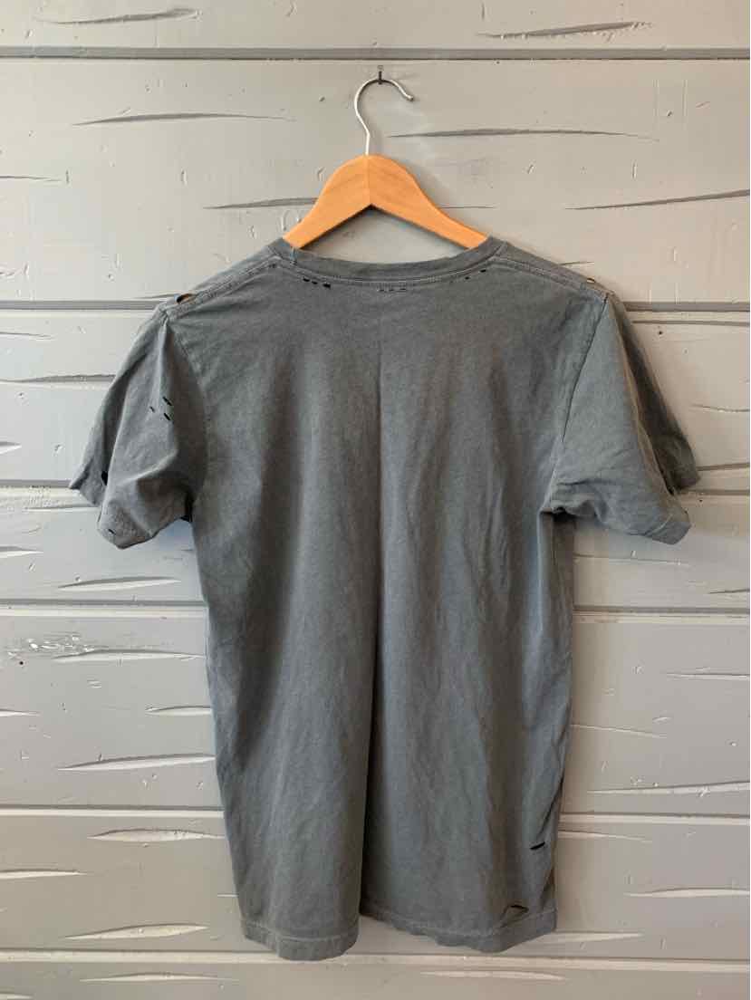 Gray short-sleeve crewneck t-shirt hanging on wooden hanger against gray wooden wall.