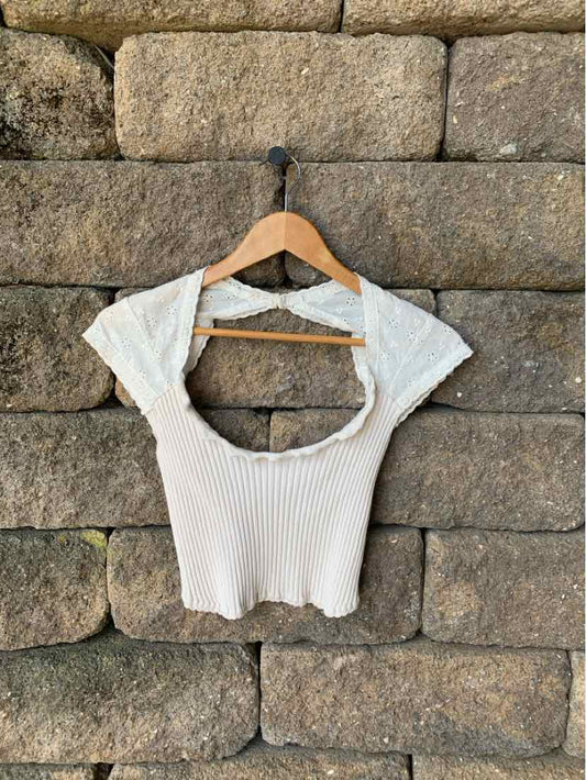 Tan ribbed knit cropped top with short sleeves and cutout back on wooden hanger.