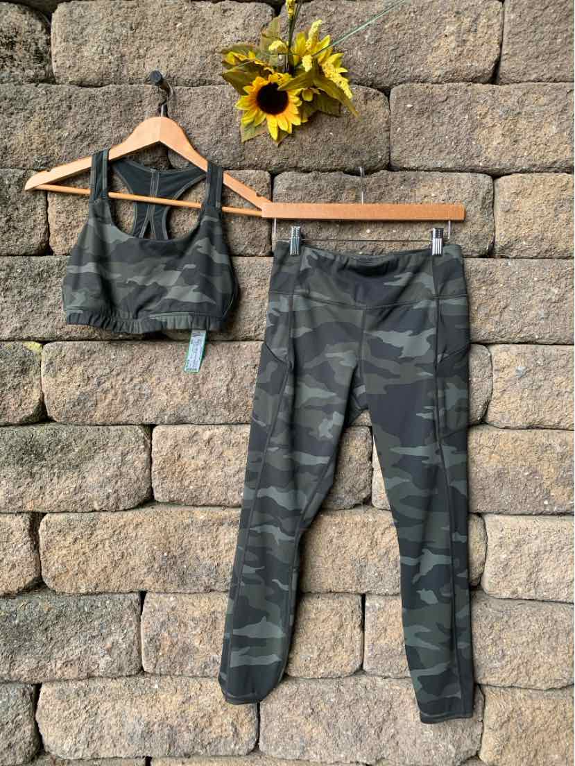 Dark green and black camo sports bra with matching high-waisted leggings on wooden hangers.