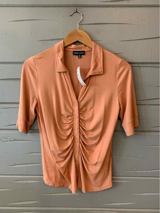 Tan short-sleeve ruched blouse with collar and button closure on wooden hanger.