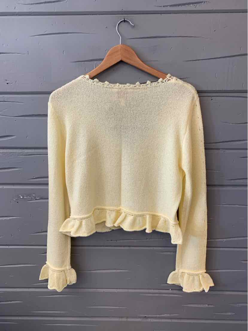 Cream knit sweater with ruffled hem and cuffs, long sleeves, and a round neckline.