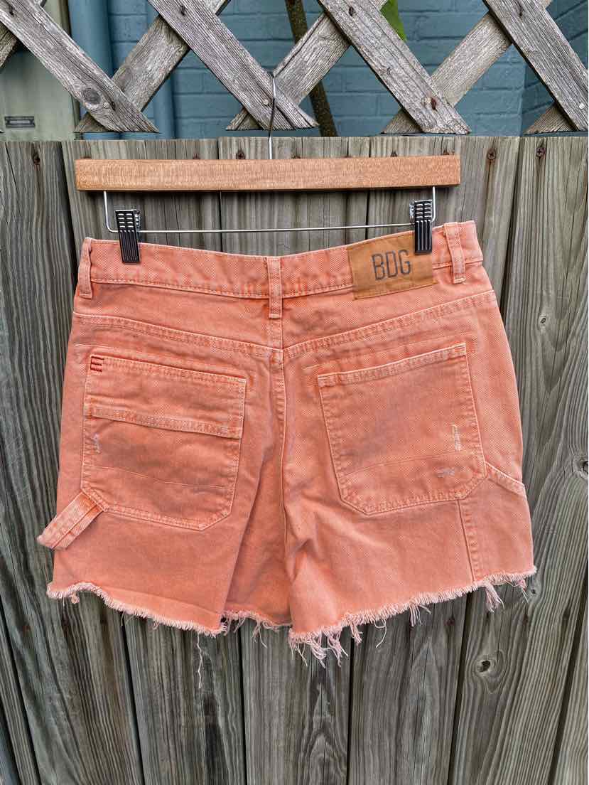 Orange denim shorts with frayed hems, back pockets, and a leather BDG patch on the waistband.