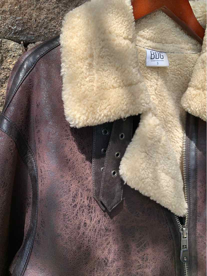 Brown distressed leather jacket with cream shearling collar and black buckle detail.