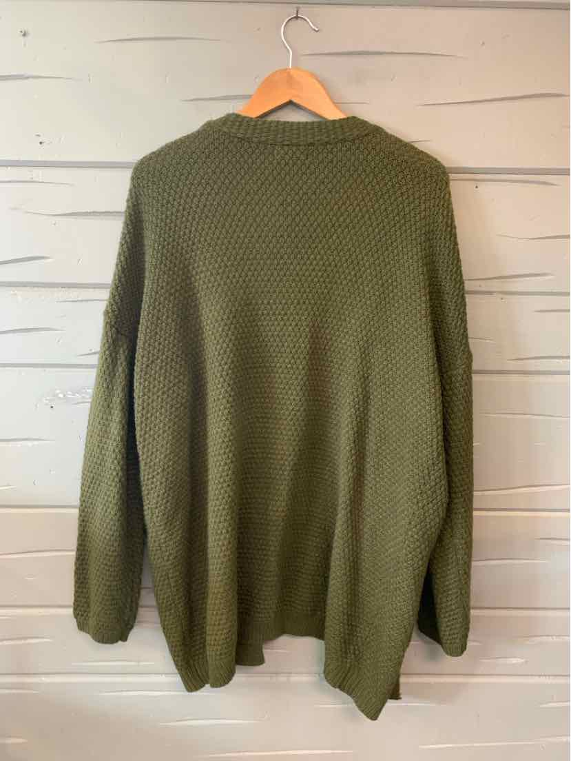 Olive green oversized knit sweater with long sleeves and textured stitch pattern hanging on wooden hanger.