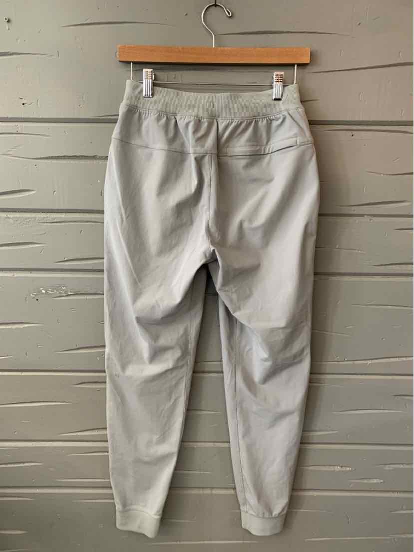 Light gray slim-fit athletic joggers with elastic waistband and cuffed ankles hanging on wooden hanger.