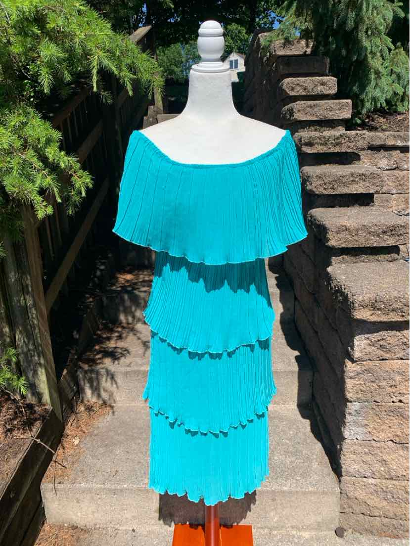 Teal knee-length dress with tiered ruffle layers and off-the-shoulder neckline on a mannequin outdoors.