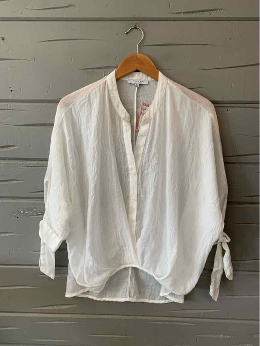 White long-sleeve blouse with loose fit, tied cuffs, and rounded hem on wooden hanger.
