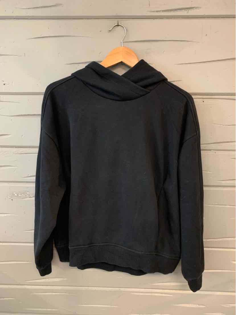 Black long-sleeve hoodie with front kangaroo pocket and ribbed cuffs and hem, hanging on wooden hanger.