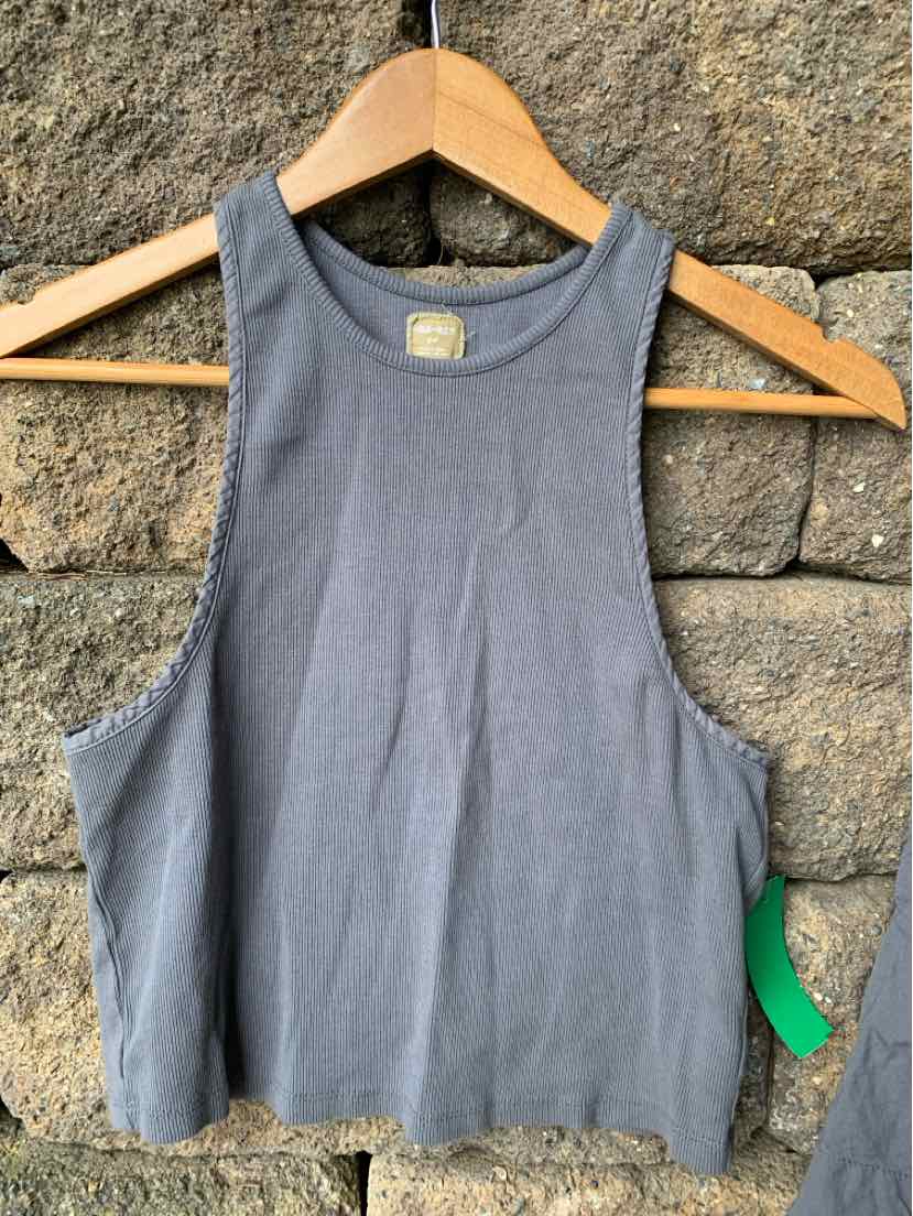 Gray sleeveless cropped tank top with high neckline on wooden hanger against stone background.