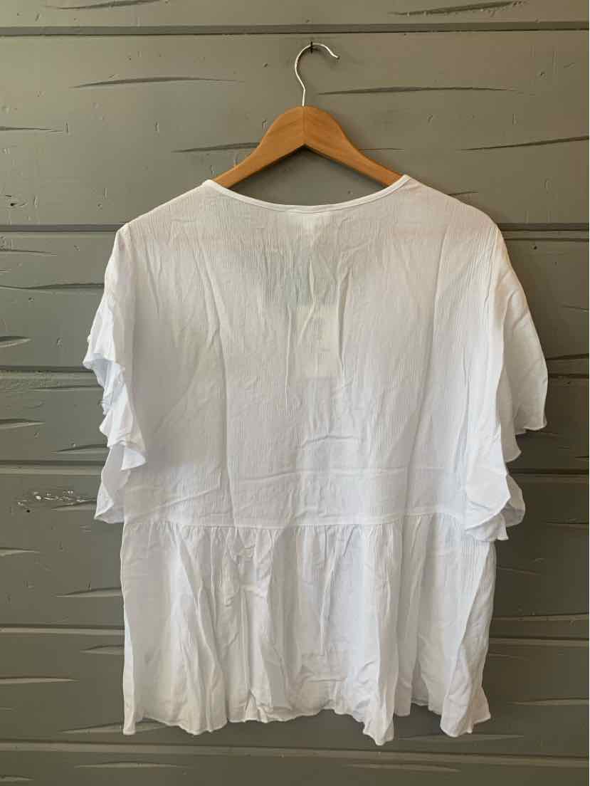 White short-sleeve blouse with ruffle details and relaxed fit, hanging on wooden hanger.
