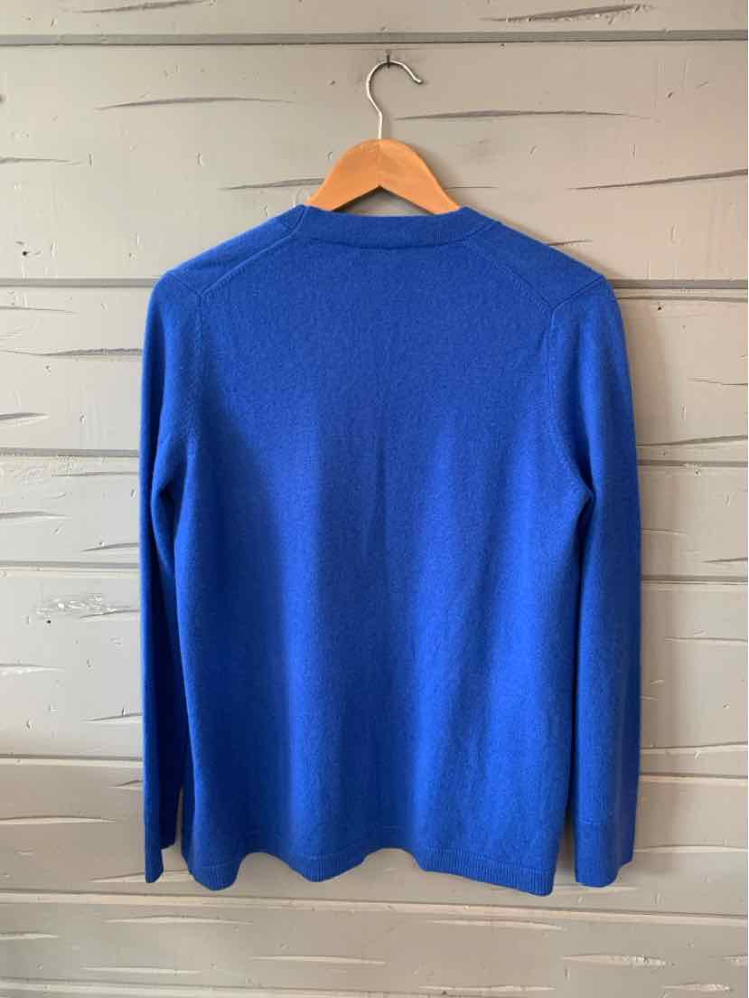 Bright blue long-sleeve sweater with a classic crew neck hanging on wooden hanger against white wood wall.