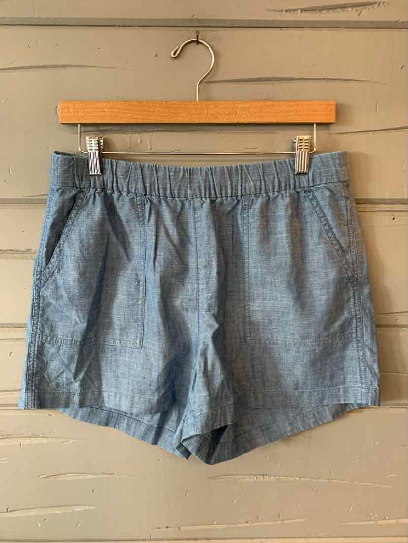 Light blue woven cotton shorts with elastic waistband and side pockets hanging on wooden hanger.