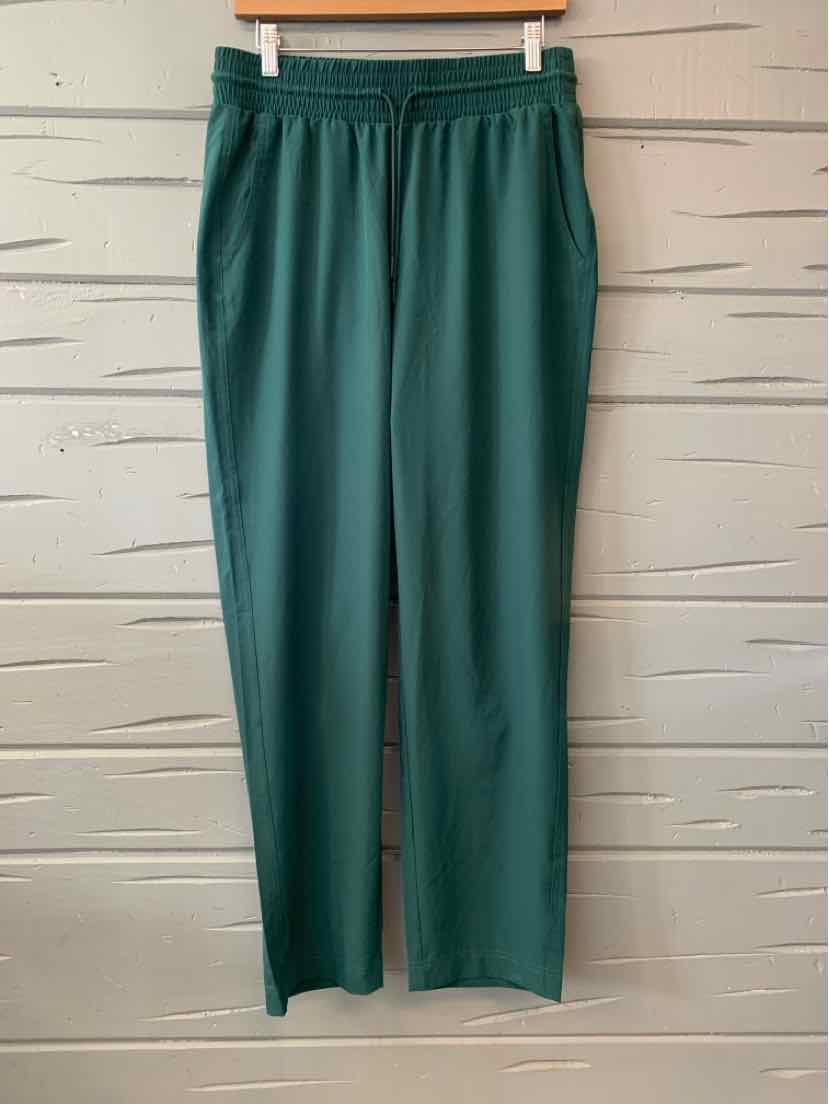 Dark green medium women's athletic pants with elastic waistband hanging against a gray patterned wall.