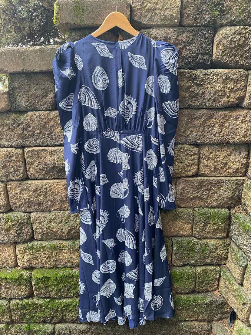 Navy blue long-sleeve dress with white seashell print, midi length, hanging on wooden hanger.