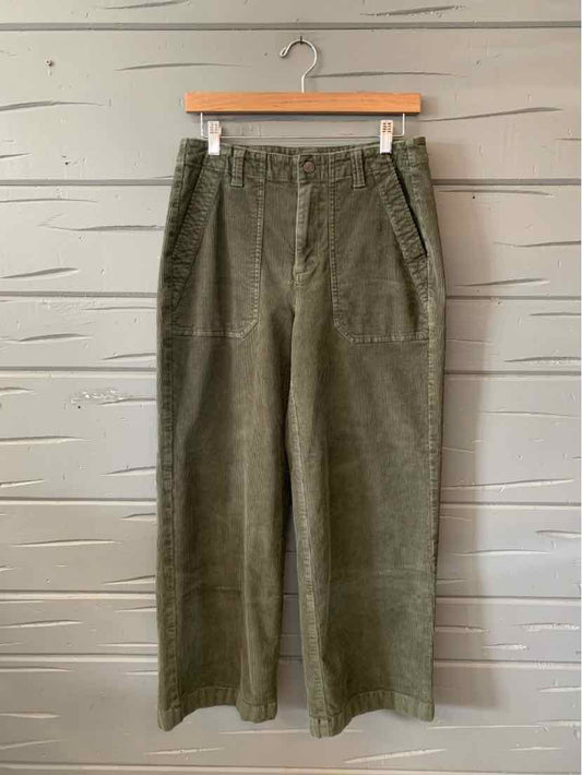 Olive green wide-leg pants with front patch pockets and belt loops hanging on wooden hanger.