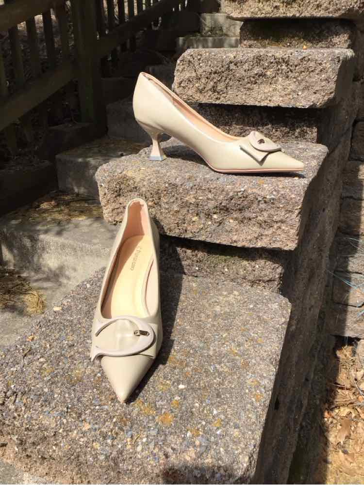 Beige pointed-toe kitten heels with bow detail on textured stone steps.