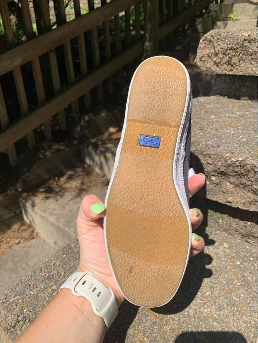Light brown rubber sole of a blue canvas sneaker with a white trim and blue Keds logo tag on the heel.