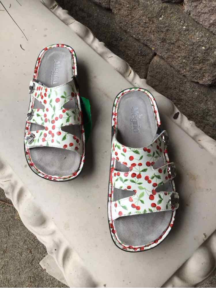 White sandals with red cherry print, adjustable double straps, and gray cushioned footbed.