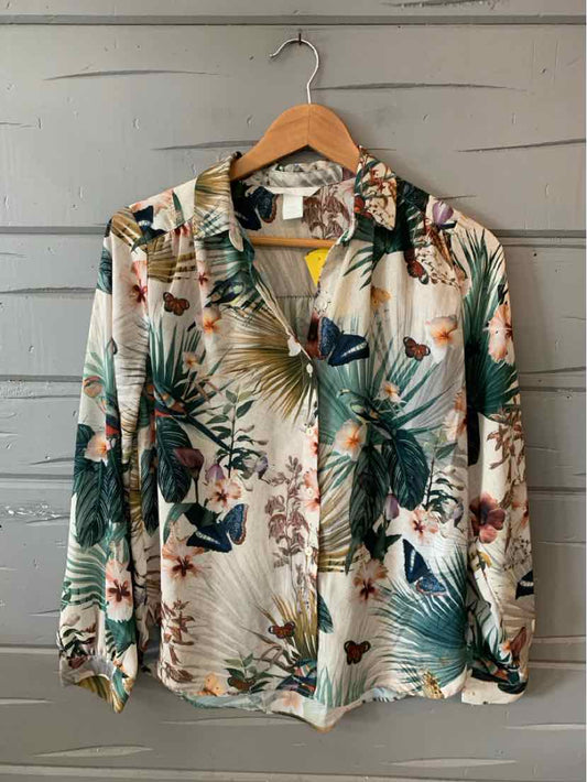 Long-sleeve button-up shirt with green and beige tropical floral print on cream fabric.