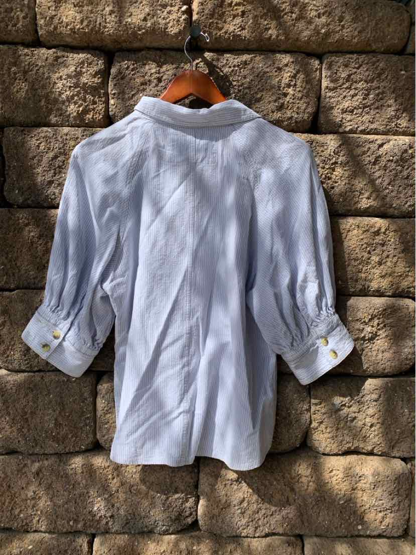 White long-sleeve blouse with buttoned cuffs and a pointed collar hanging against a stone wall.