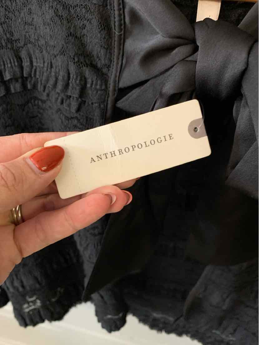 Black lace garment with layered ruffles and a cream Anthropologie tag held in front.