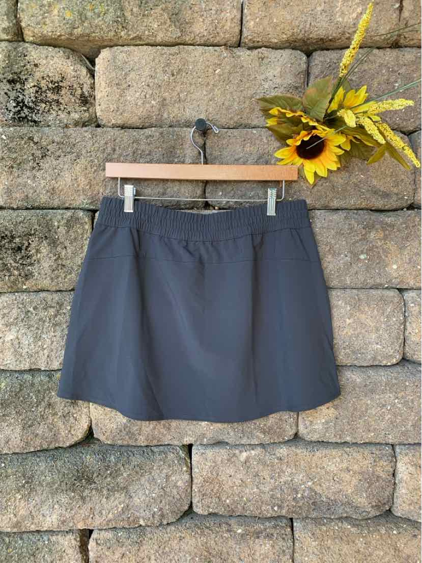 Dark gray athletic skirt with elastic waistband hanging on wooden hanger against stone wall background.
