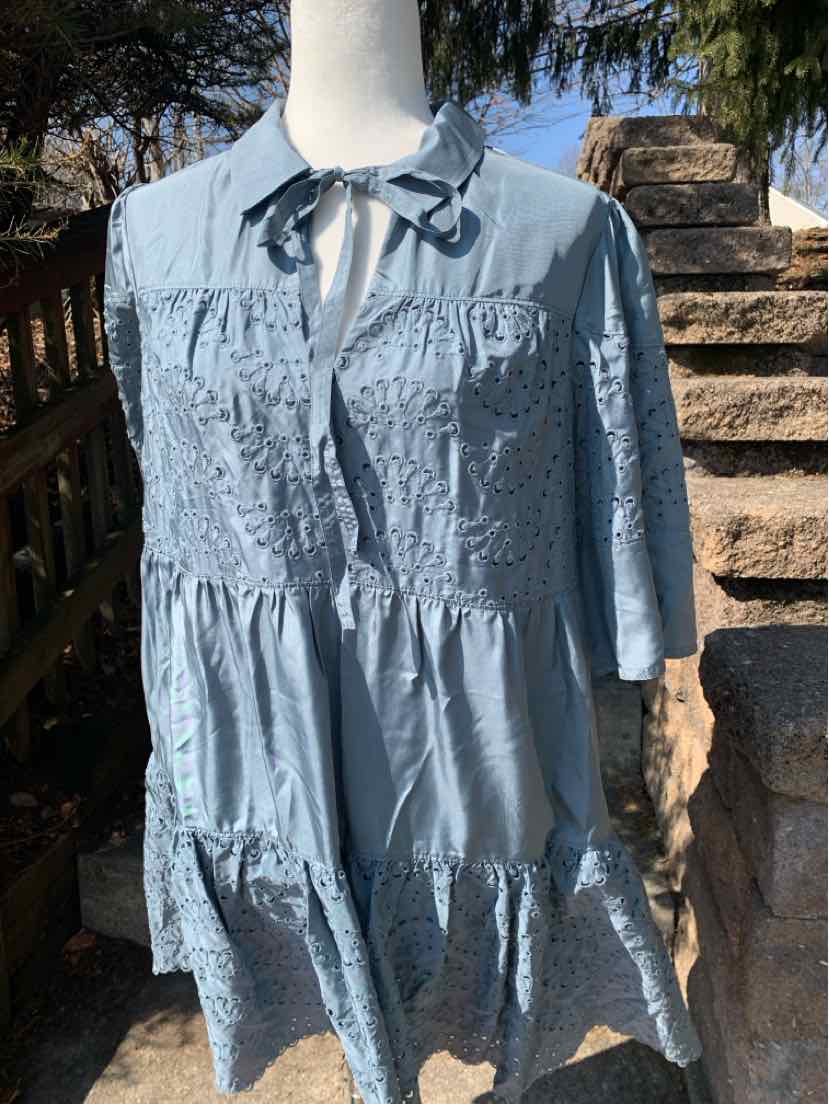 Light blue tiered eyelet dress with three-quarter sleeves and a tie neck collar on mannequin.