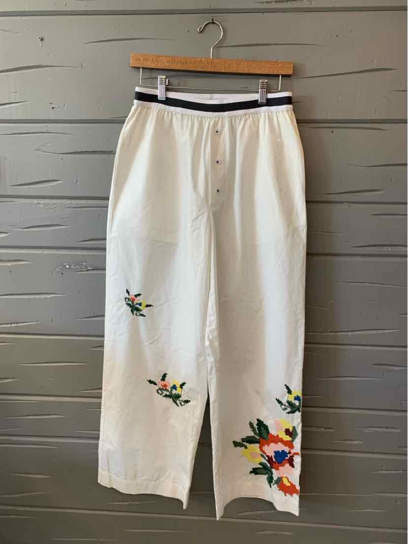 White wide-leg pants with embroidered colorful floral designs near the hem and a black-striped elastic waistband.