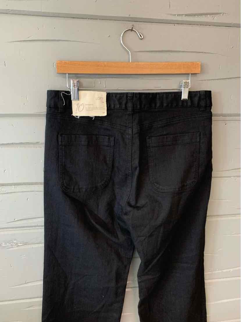 Black denim jeans size 10 with back pockets and leather patch on waistband hanging on wooden hanger.