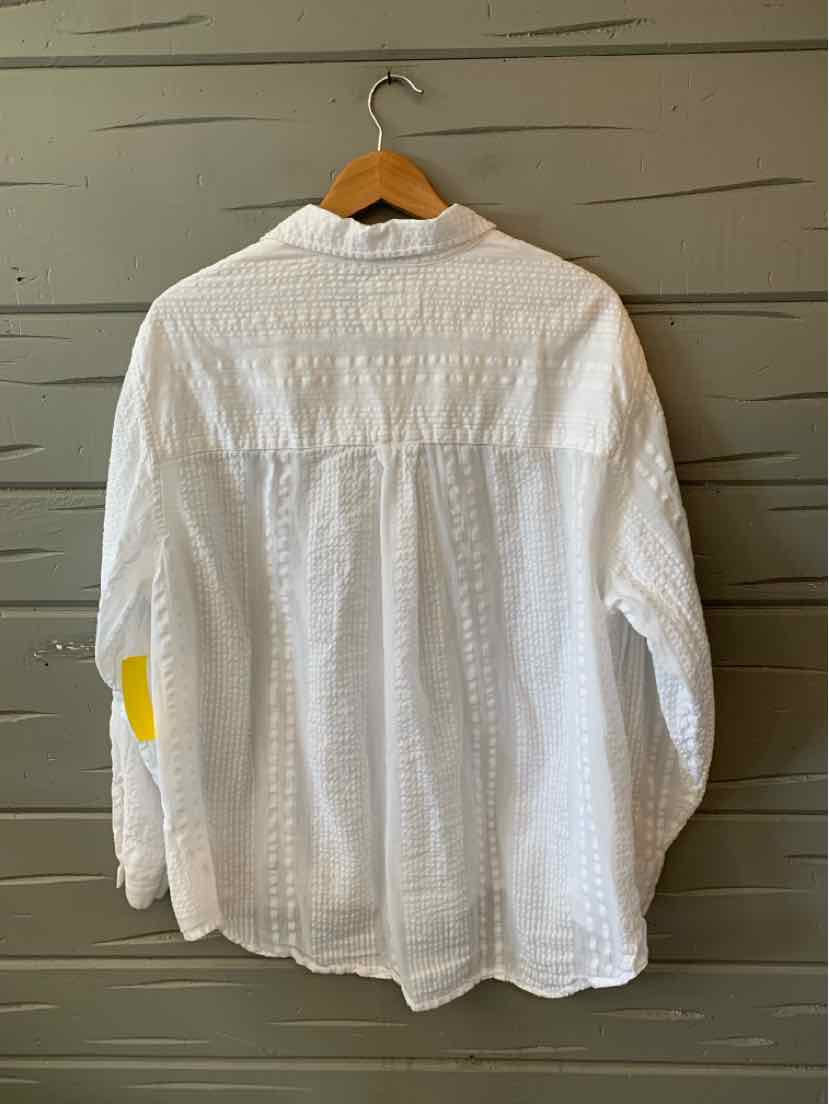White long-sleeve button-up shirt with textured fabric and relaxed fit hanging on wooden hanger.