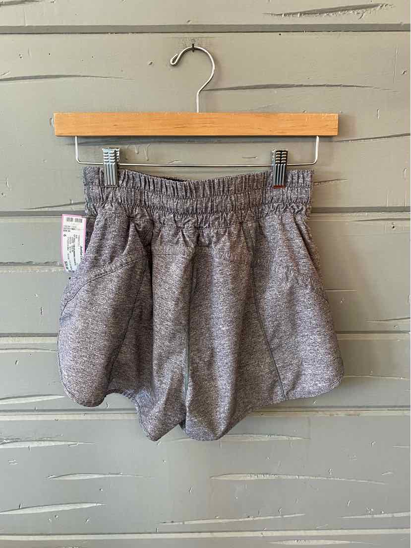 Heather gray athletic shorts with elastic waistband and side pockets hanging on wooden hanger against gray wooden wall.